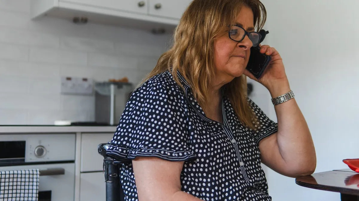 Person in a wheelchair checking a loan e-transfer on a phone in a kitchen